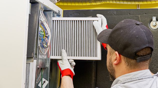An HVAC service technician replaces an air conditioner filter