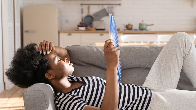 Person laying on couch, cooling themselves with a handheld fan.