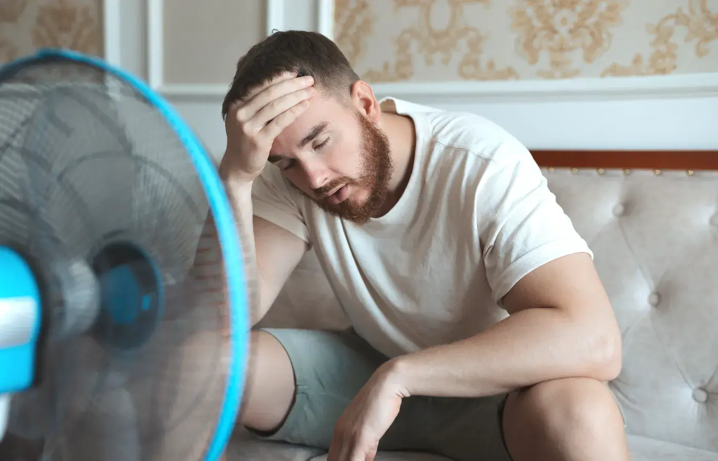 Air Conditioning Repair Person sitting uncomfortably hot on couch in front of fan