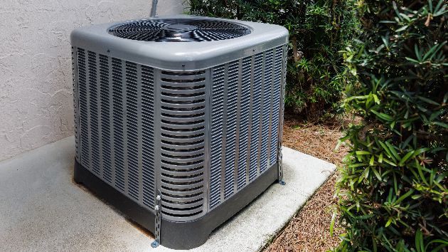 Outdoor air conditioning unit sitting on pavement in a household yard.